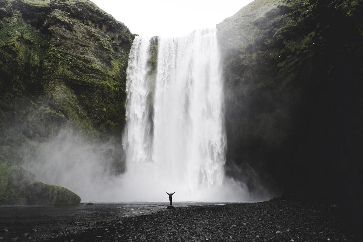 Mensch steht vor meterhohem Wasserfall in Island