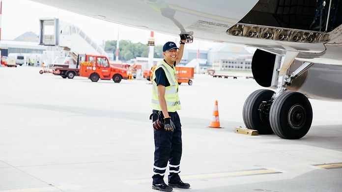 Mitarbeiter vom Groundhanling in Arbeitskleidung greift in Klappe unter dem Flugzeugrumpf