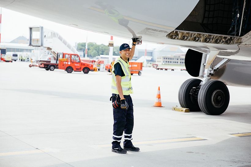 Mitarbeiter vom Groundhanling in Arbeitskleidung greift in Klappe unter dem Flugzeugrumpf