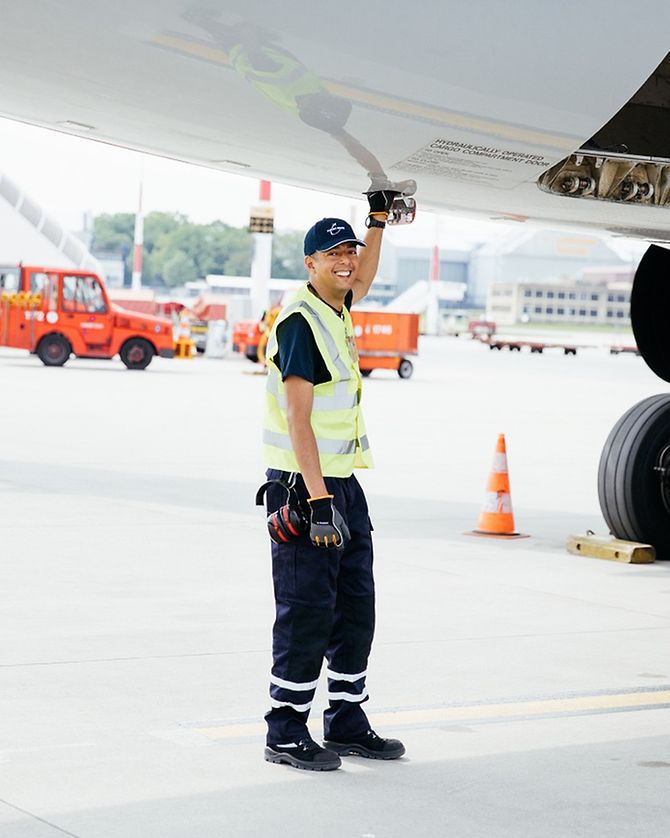 Mitarbeiter vom Groundhanling in Arbeitskleidung greift in Klappe unter dem Flugzeugrumpf