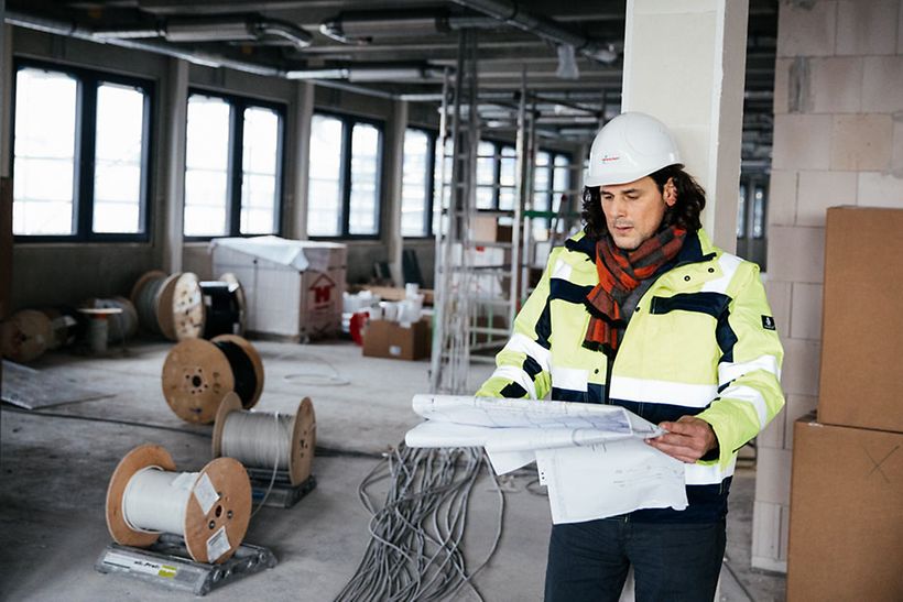 Ein Mitarbeiter mit Schutzhelm liest Bauplan auf einer Baustelle