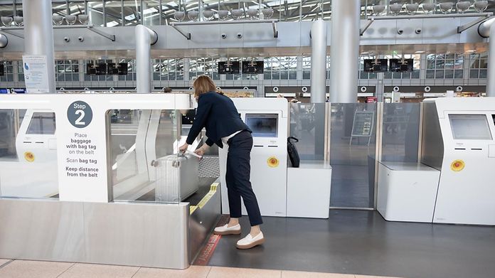 Frau steht vor dem Self-Bag-Drop-Automaten und legt ihr Gebäckstück auf der Seite liegend auf das Kofferband.