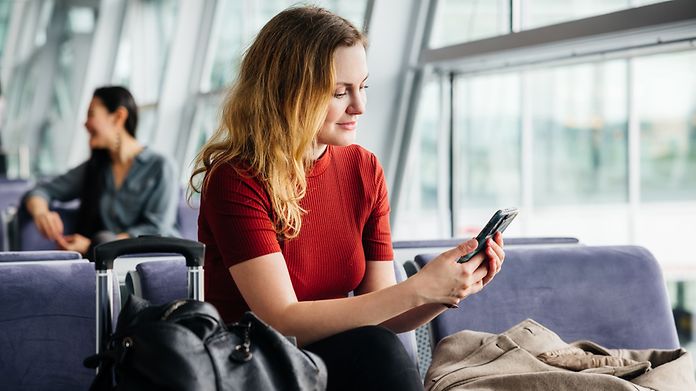 Frau wartet mit Handy in der Hand am Gate auf den Abflug.