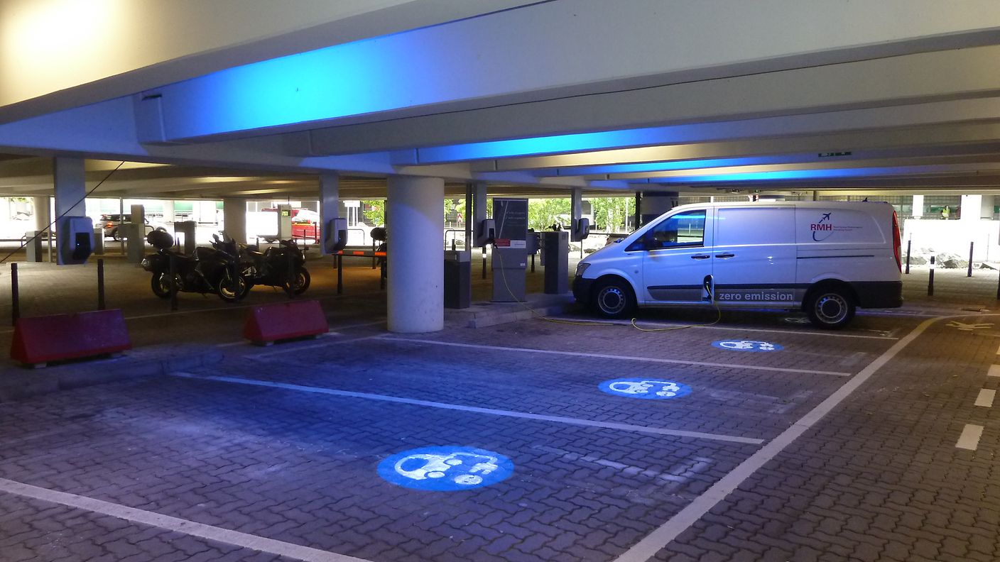 Parking spaces for electric cars are marked with a blue logo on the ground.