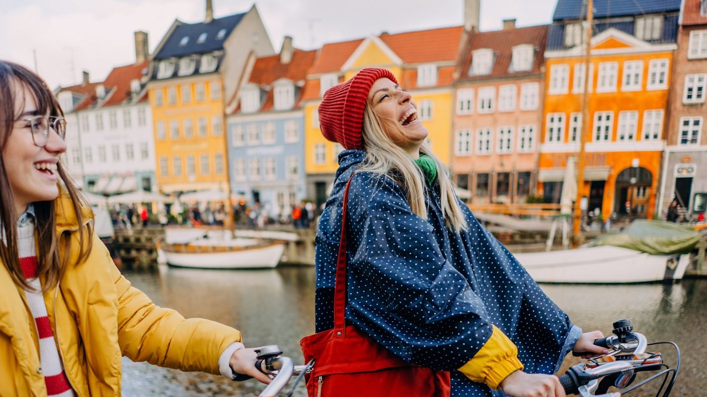 Junge Frauen fahren lachend mit dem Fahrrad durch Kopenhagen