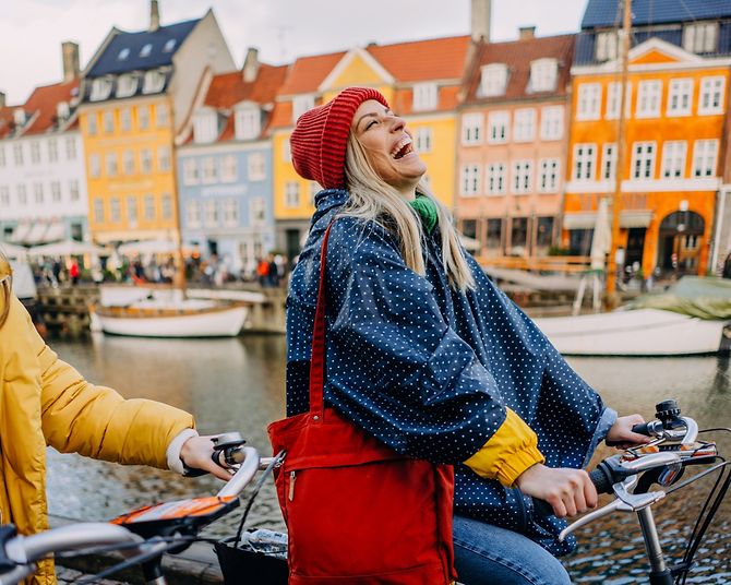 Junge Frauen fahren lachend mit dem Fahrrad durch Kopenhagen