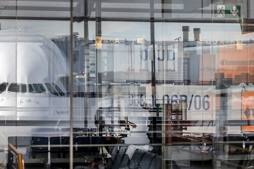 Ein Flugzeug und Frachtcontainer spiegeln sich in der Scheibe des Flughafen-Terminals