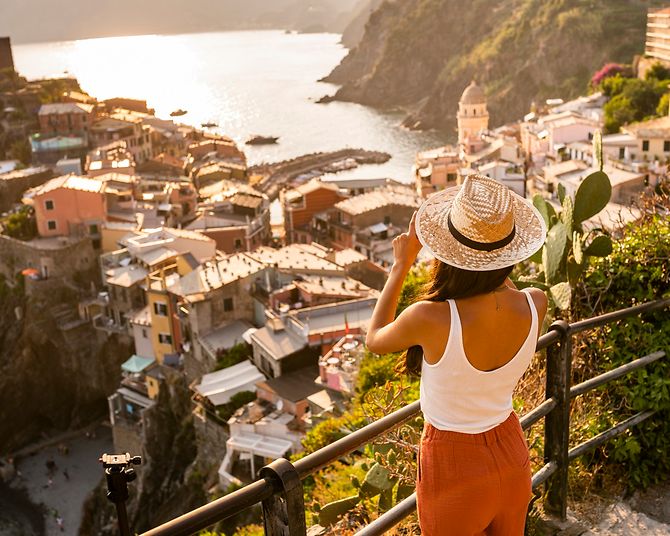 Frau mit Sonnenhut sieht im Urlaub von einem Berg auf eine Altstadt