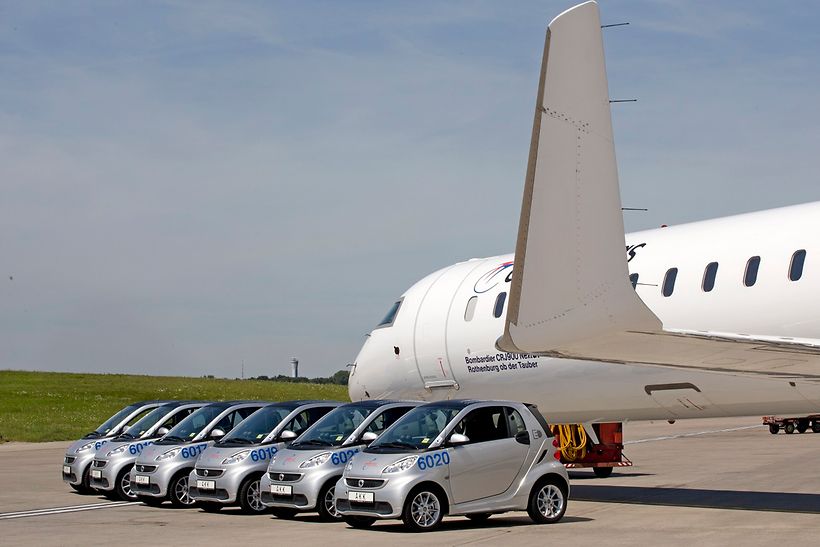 Elektro-Autos auf dem Vorfeld des Hamburg Airport neben einem Flugzeug.