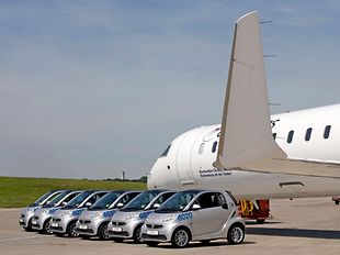 Elektro-Autos auf dem Vorfeld des Hamburg Airport neben einem Flugzeug.