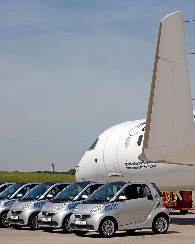 Elektro-Autos auf dem Vorfeld des Hamburg Airport neben einem Flugzeug.