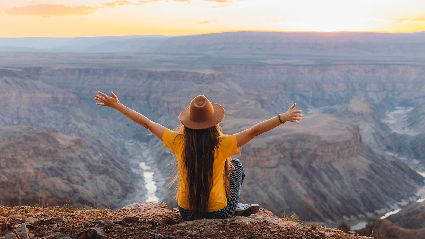 Eine Frau sitzt mit ausgebreiteten Armen am Fish River Canyon in Namibia