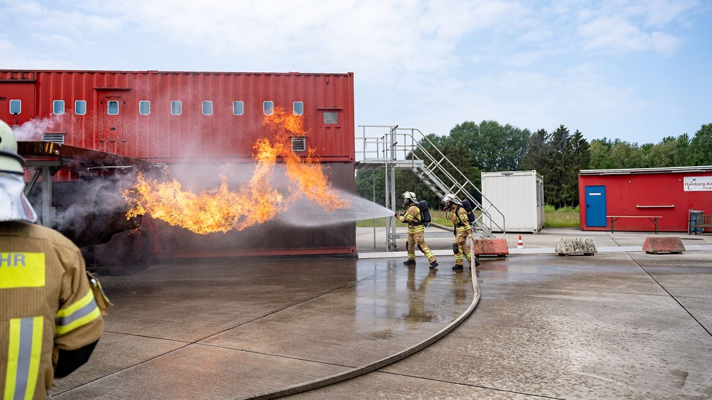 Zwei Feuerwehrleute löschen mit dem Wasserschlauch ein Feuer.