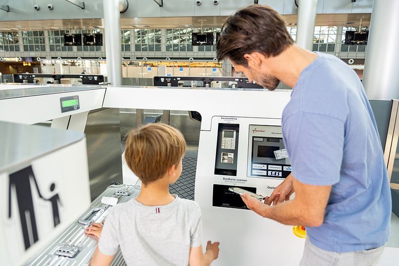 Ein Vater und sein Sohn geben einen Koffer am Self-Bag-Drop-Automaten ab