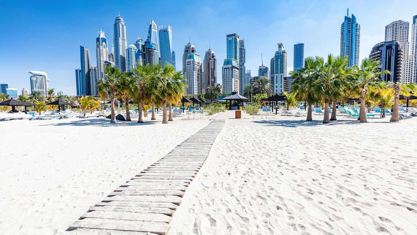 Strand mit Palmen in Dubai vor der Skyline aus Wolkenkratzern
